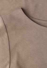 Beżowa bawełniana tkanina o gładkiej fakturze, z okrągłym dekoltem i nakładającym się szwem, przedstawiona na zdjęciu z bliska.