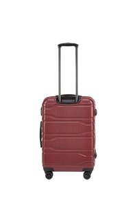 Valise rigide rouge avec surface texturée, poignée rétractable, quatre roues et design élancé. Rainures notables pour une meilleure prise.