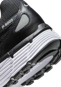 Juodos Nike P-6000 sneakerio kulnas su tekstūruota tinkleliu, sintetiniais intarpais ir balta banguota padanga. Yra subtilūs pilki akcentai ir ženklai.