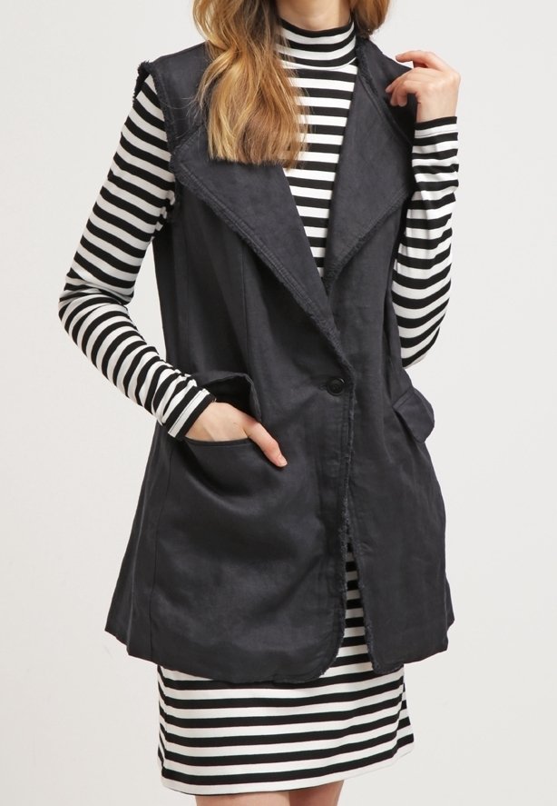 Gilet sans manches noir avec un col châle, comportant deux poches avant et une fermeture à bouton unique, superposé sur une robe rayée noir et blanc.