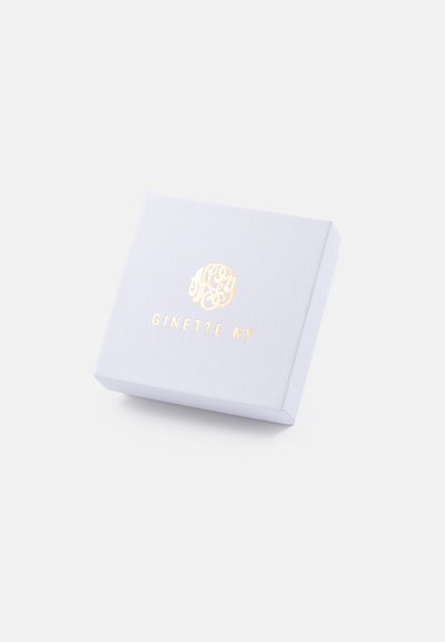 Boîte à bijoux blanche texturée avec un logo en feuille d'or "GINETTE NY" à l'avant, de forme carrée, fermée avec des bords vifs.