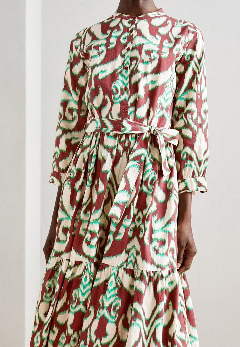 Vestito a maniche lunghe con motivo astratto rosso, verde e crema, chiusura frontale con bottoni e cintura in vita annodata.