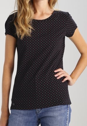 Woman wearing a fitted black short-sleeve shirt with small red and white polka dots, paired with blue jeans.