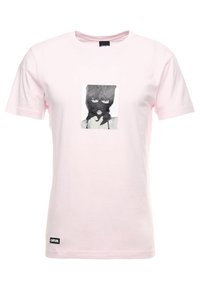 Camiseta de algodón de color rosa claro con un gráfico central en blanco y negro de una persona con pasamontañas, con mangas cortas y un cuello redondo.