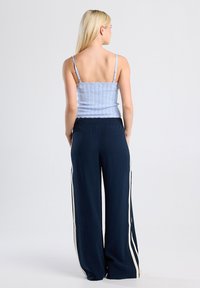 Light blue, ribbed crop top with thin straps paired with dark navy wide-leg pants featuring white side stripes. Smooth fabric texture.