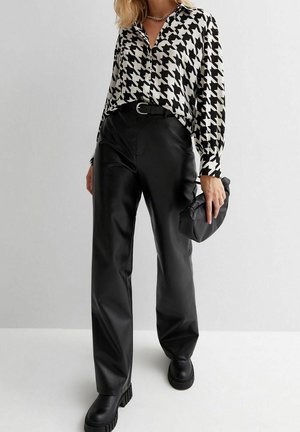 Zwart-witte pied-de-poule blouse gecombineerd met zwarte nep leren broek en stevige zwarte laarzen. Accessoires omvatten een kleine zwarte clutch.