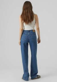 Jeans blue cu talie înaltă, cu croială dreaptă, având o etichetă din piele pe talie și două buzunare pe spate.