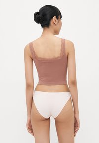 Bruine cropped top met kantafwerking en verstelbare bandjes, gecombineerd met lichtroze naadloze ondergoed. Soepele textuur, nauwsluitende vorm.
