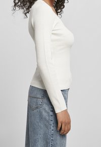 Biała prążkowana bluzka z długim rękawem, z dekoltem w kształcie litery V. Do tego niebieska spódnica dżinsowa o prostym kroju z tylną kieszenią.