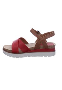 Red and brown sandal with a cork insole, cross-strap design, adjustable ankle buckle, and a white rubber sole.