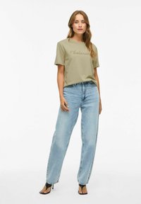 Olijfgroene T-shirt met de tekst "balans", gecombineerd met lichtblauwe denim jeans. De outfit heeft korte mouwen en een relaxte pasvorm.