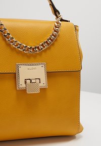 Sac à main en similicuir jaune avec une bandoulière chaîne dorée brillante et une fermeture à verrou carré à motif texturé.