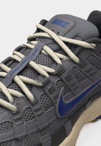 Γκρι αθλητικό παπούτσι Nike Air Jordan Series με μπεζ κορδόνια, μπλε λογότυπο swoosh και επάνω μέρος από πλέγμα.