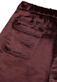 Bordo satininiai šortai turi elastingą juosmenį ir užpakalinę kišenę su įspaustu logotipu. Medžiaga pasižymi blizgiu, tekstūriniu paviršiumi.