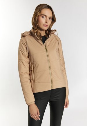 Lichtbruin gewatteerd jack met een capuchon, gouden rits en geribbelde manchetten. Heeft een gequiltde structuur en zijzakken. Draagt over zwarte broek.
