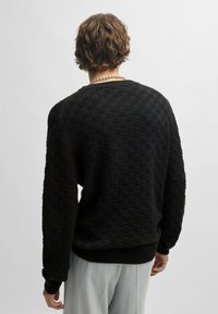 Schwarzer strukturierter Pullover mit einem Karomuster, gerippten Ärmeln und Saum. Das Design verfügt über einen klassischen Rundhalsausschnitt und einen lässigen Schnitt.