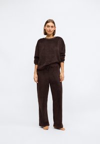 Hnědá fleecová mikina a odpovídající kalhoty, volný střih, kulatý výstřih, dlouhé rukávy, texturovaná látka, pas na stahování, měkký vzhled.