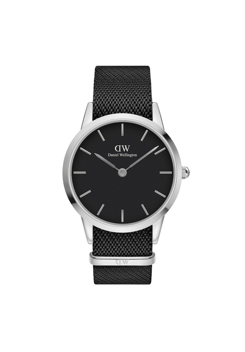 Must mustriba kell, millel on ümara kujuga roostevabast terasest korpus, must hind, hõbedased tunni markerid ja brändi nimi "Daniel Wellington".