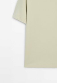 T-shirt en coton beige clair à manches courtes avec coutures visibles sur la manche et l'ourlet sur fond blanc.