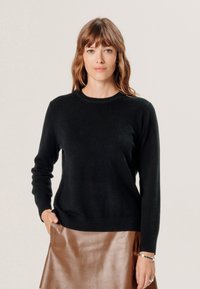 Zwarte trui met ronde hals en lange mouwen, gemaakt van zachte stof; gecombineerd met een glanzende bruine leren rok, met een gladde textuur en elegante pasvorm.