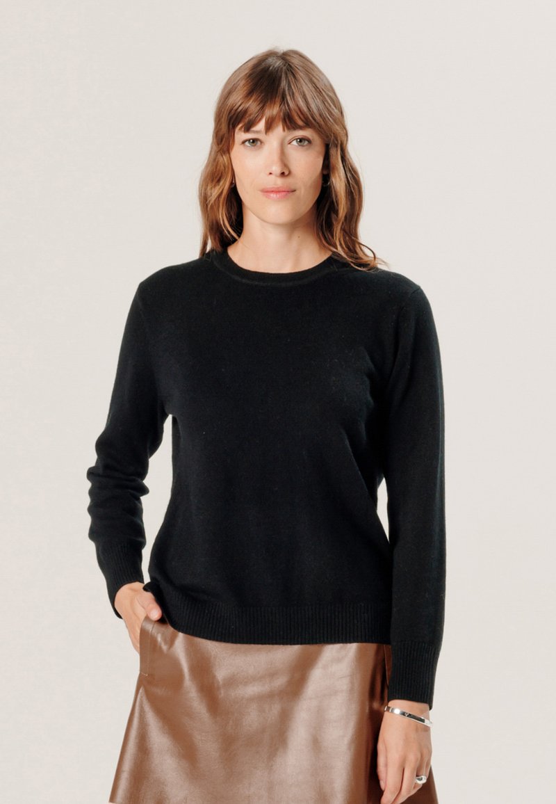 Zwarte trui met ronde hals en lange mouwen, gemaakt van zachte stof; gecombineerd met een glanzende bruine leren rok, met een gladde textuur en elegante pasvorm.