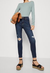 Jasnoniebieska bluzka z długim rękawem, ciemnoniebieskie jeansy skinny z wysokim stanem z dziurami oraz czarne espadryle na platformie z plecionymi detalami.