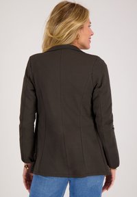Bruine, getailleerde blazer met lange mouwen, gestructureerde kraag en zijzakken. De gladde textuur en op maat gemaakte naden benadrukken de silhoutte.