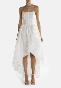 Hvid strapless kjole med tætsiddende liv og lagdelt høj-lav skørt. Blødt, let stof; glat tekstur, minimalistisk design. Sølv sandaler.