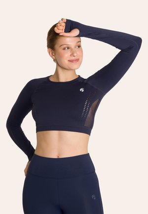 Marineblauw crop top met lange mouwen, voorzien van ademende meshpanelen, ronde halslijn en versterkte stiksels. Gecombineerd met bijpassende hoog-waisted legging.