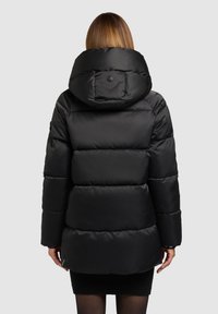 Must pufferjope, millel on suur kapuuts, tikitud sektsioonid ja sile, läikiv pind. Hääle lähedal on logomärk.