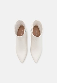 Paire de bottines blanches à bouts pointus avec fermetures éclair latérales, vues de dessus sur un fond clair.