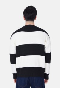 Maglione a righe bianche e nere con un design a maglia testurizzata, maniche lunghe e orlo a costine. Vista posteriore mostrata.