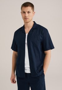 Camisa de manga corta azul marino de tela ligera, con cuello, botonadura frontal y bolsillo en el pecho izquierdo. Textura suave.
