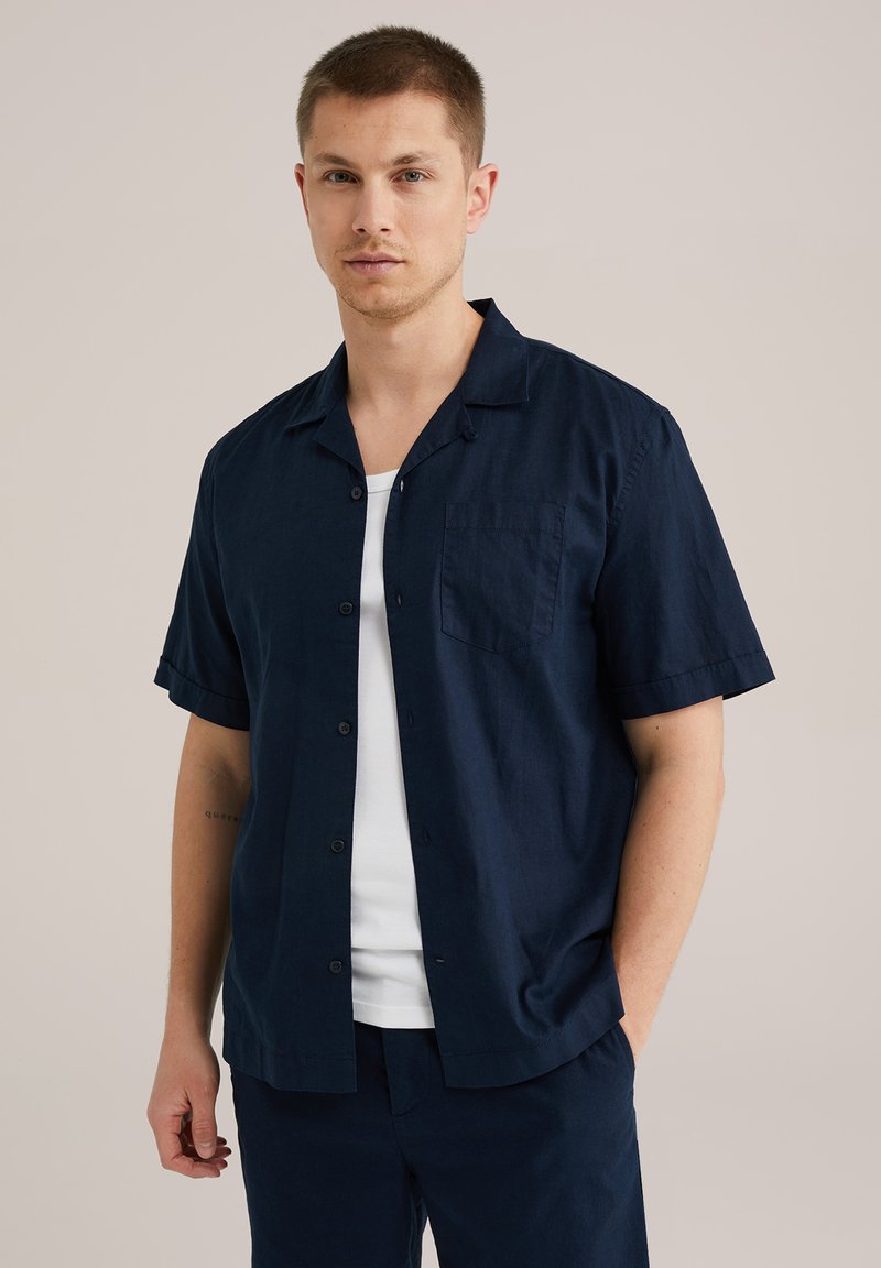 Camisa de manga corta azul marino de tela ligera, con cuello, botonadura frontal y bolsillo en el pecho izquierdo. Textura suave.