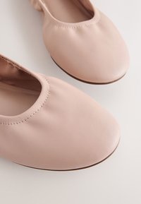 Ballerines en cuir rose doux avec bouts arrondis et bords élastiqués, présentées en gros plan sur un fond clair.