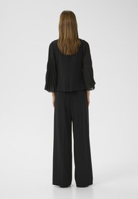 Top nero a maniche lunghe con dettagli plissettati abbinato a pantaloni neri larghi. Tessuto liscio, design minimalista e senza motivi visibili.