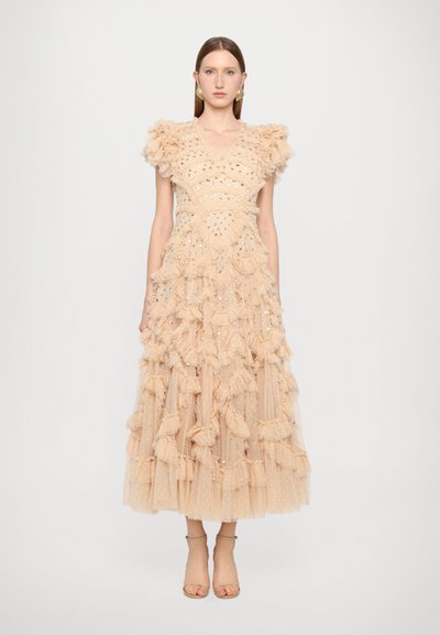Robe en tulle beige avec des volants superposés, dotée d'un décolleté en V et d'accents métalliques, accompagnée de sandales à lanières simples.