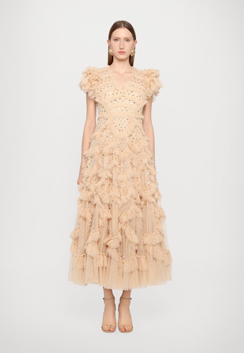 Robe en tulle beige avec des volants superposés, dotée d'un décolleté en V et d'accents métalliques, accompagnée de sandales à lanières simples.