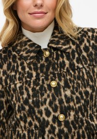 Giacca con stampa leopardata in beige e nero, con chiusure a bottoni dorati e colletto. Il tessuto sembra morbido con una finitura strutturata.