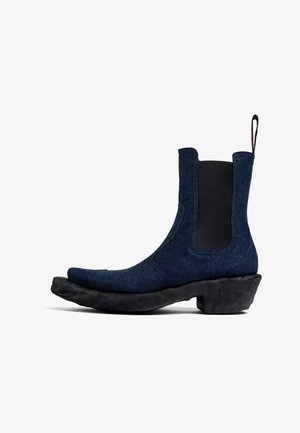 Jeansowe botki na kostkę z krzywą, grubą czarną podeszwą; elastyczne boczne panele; spiczasty kształt czubka; ciemnoniebieski kolor; pętla do zakładania z tyłu.