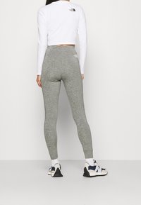 Šedé legíny z elastického materiálu, vyrobené z měkké tkaniny, s vysokým pasem a logem The North Face na zadní straně. Nosí se s bílým cropped topem a teniskami.