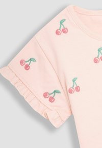 Lyserød bomuld t-shirt med korte, voluminøse ærmer. Har broderede kirsebær i pink og grøn på ærmerne og kroppen.