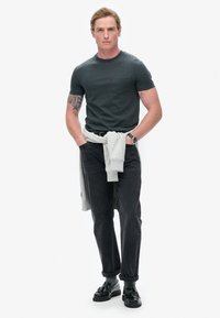Mørkegrå bomulds T-shirt med lomme, parret med sorte denim jeans. En lys grå sweatshirt hængende om livet, båret med sorte sko.