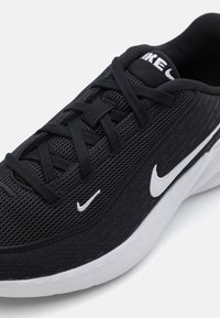 Crne sportske tenisice s mrežastim gornjištem, bijelim akcentima i teksturiranom potplatom. Imaju vezice i Nike logotip na jeziku i bočnoj strani.