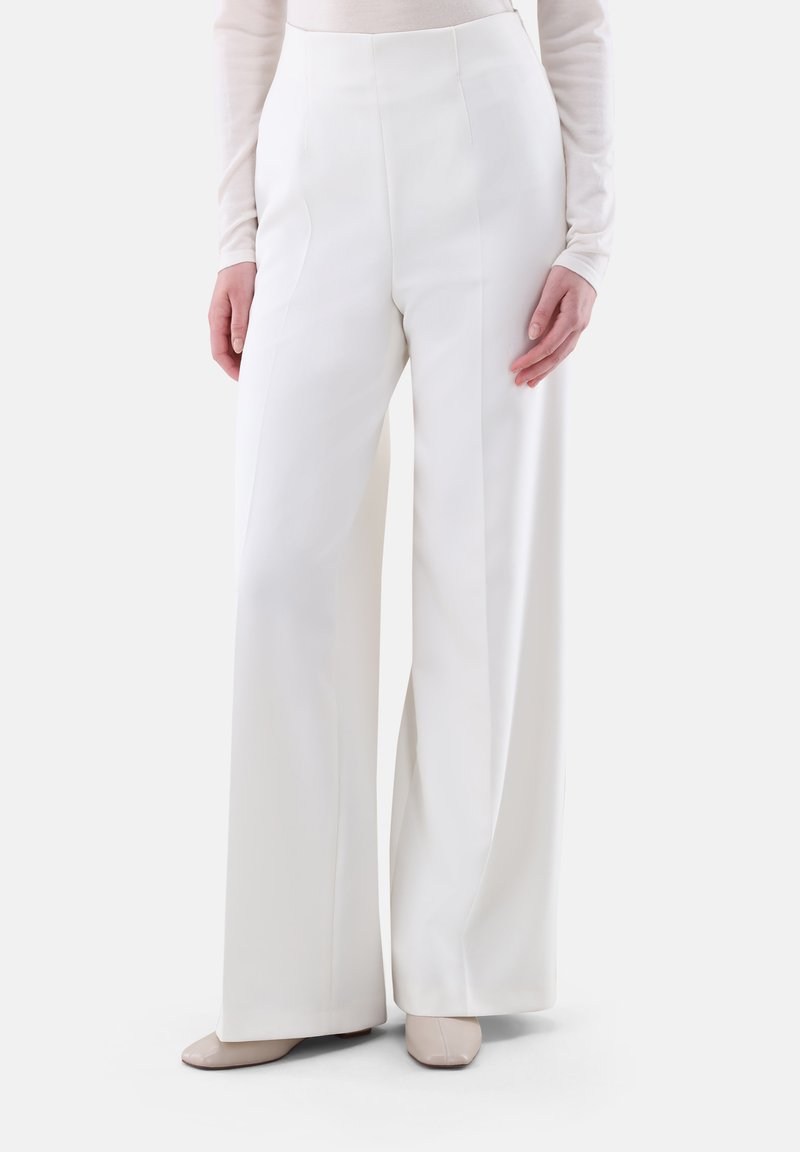 Weiße, weite Hose mit hohem Bund, glatter Textur und klaren Linien. Kombiniert mit hellen Schuhen. Maßgeschneidertes Design.