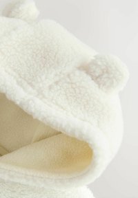 Weißer Fleece-Hoodie mit weicher, flauschiger Textur und runden Pompons an der Oberseite. Das Innenfutter ist in einer helleren Cremefarbe gehalten.