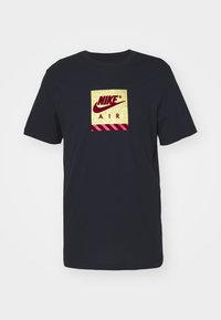 Μαύρο βαμβακερό T-shirt με κεντρικό χρυσό και μπορντό σχέδιο Nike Air μέσα σε τετράγωνο, με διαγωνίες γραμμές στη βάση.