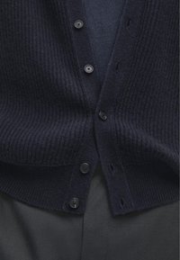 Cardigan ribattuto blu navy con sei bottoni neri e design a V. Il materiale è texturizzato con un aspetto morbido e lavorato a maglia.