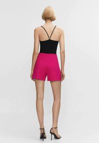 Zwarte spaghetti-top met roze high-waisted shorts. De shorts hebben een gladde stof en een klassieke snit, met twee achterzakken.