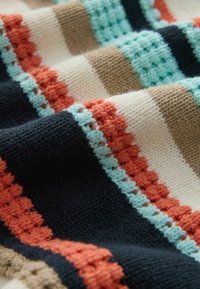 Nahaufnahme eines gestrickten Stoffs mit horizontalen Streifen in Schwarz, Beige, Creme, Orange und Hellblau mit verschiedenen Strickmustern.